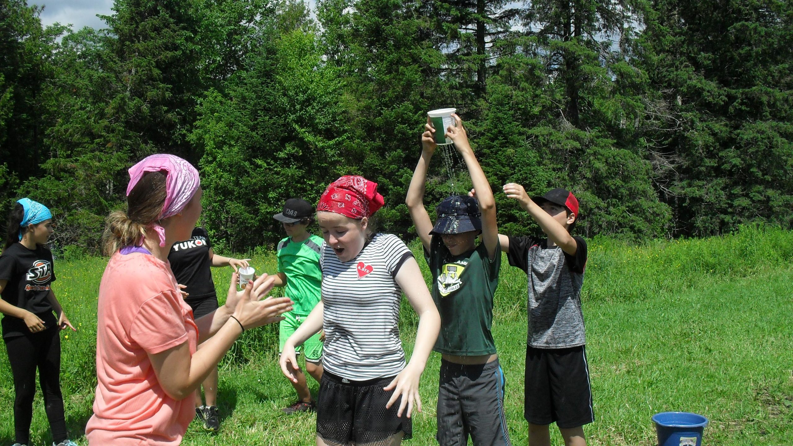 5 jeunes éclaireurs de la troupe des Harfangs des neiges se rafraîchissant avec des bols d'eau lors d'un camp d'été.