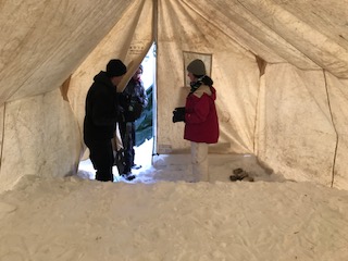 Deux éclaireurs dans une tente prospecteur en tissus bâche, avec un bloc de neige pour servir de coupe-vent