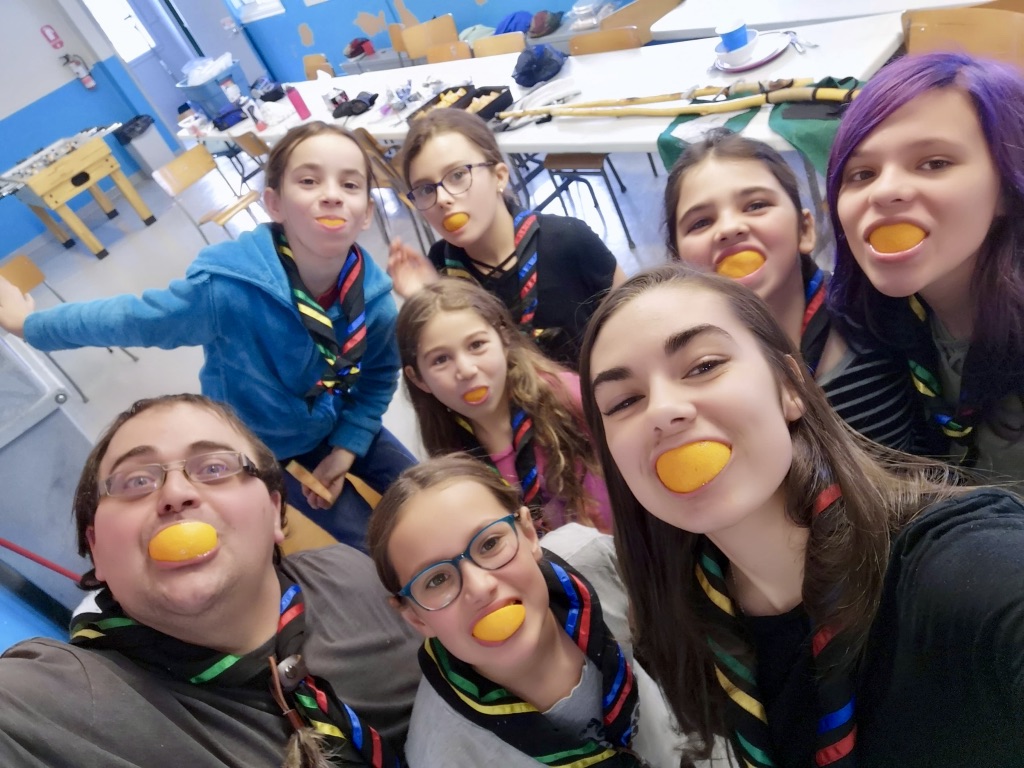 6 jeunes filles de l'unité des Chouettes (filles, 9-11 ans) et 2 animateurs faisant la grimace avec un quartier d'orange à la place des dents.